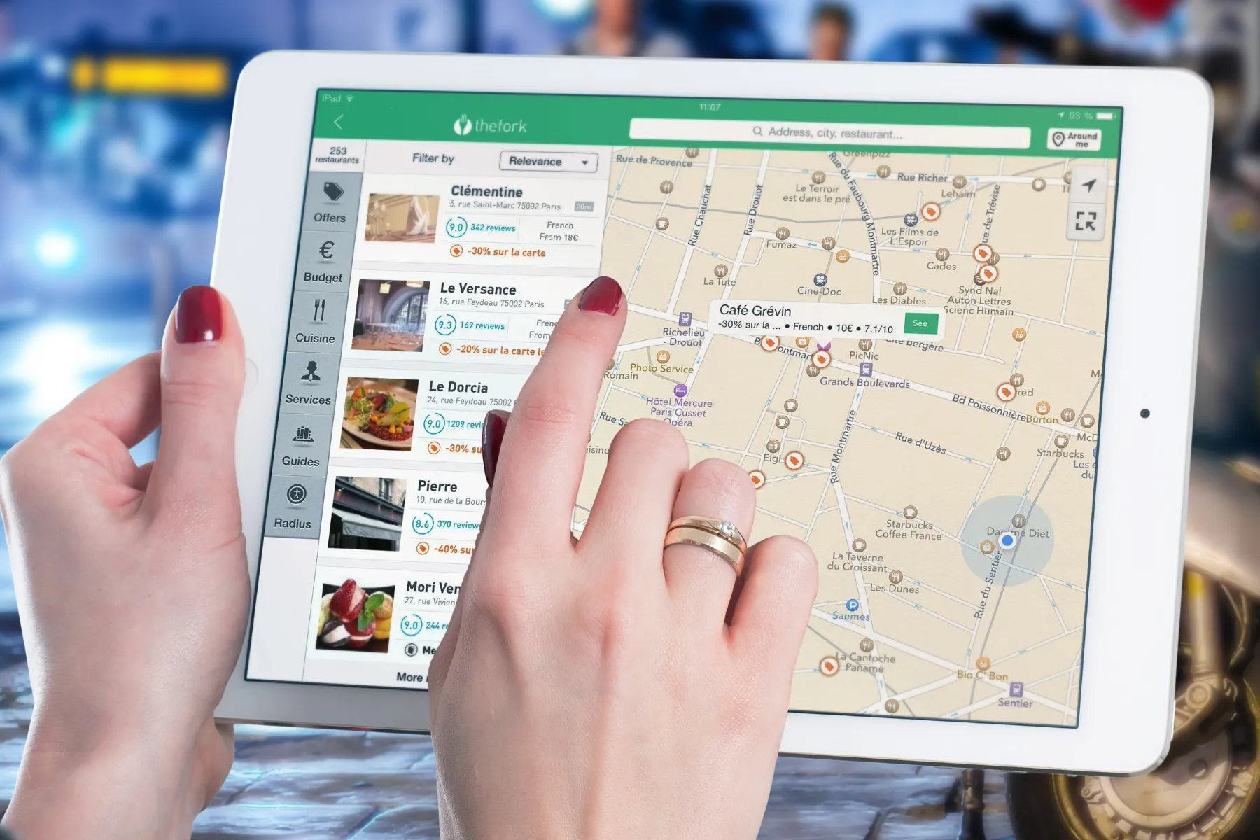 A woman interacting with a digital map application on a tablet searching for French restaurants in the place