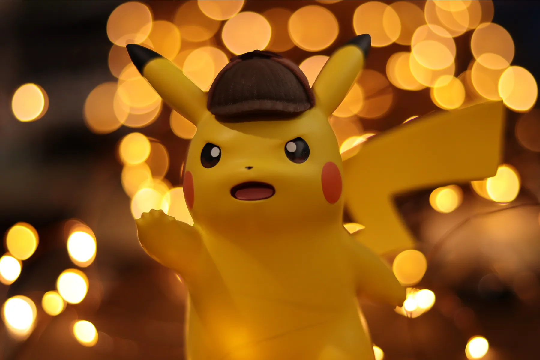Close-up of a Pikachu toy wearing a detective-style hat with warm golden lights in the background.